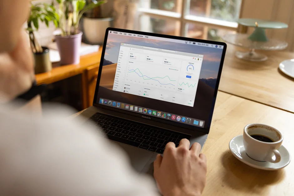 Person analyzes stock data with a smartphone and laptop, indoors.
